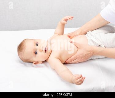 Six month baby girl receiving massage therapy in pediatric clinic. Manual therapist manipulates child's abdomen and chest Stock Photo