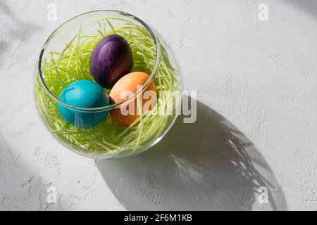 Glass bowl with edible candy grass and three colorful easter eggs (blue, purple and orange,) Stock Photo