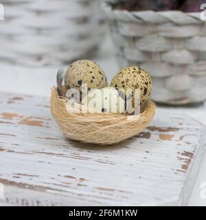Three quail eggs in a nest on a white cutting board on concrete. Easter concept. Close-up. Stock Photo