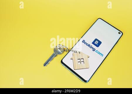 SWANSEA, UK - MARCH 31, 2021: Booking.com app logo displayed on smartphone, home key with house keyring on yellow background with copy space Stock Photo
