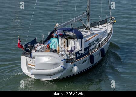 a man at the helm of a large racing or cruising yacht steering the boat trough a channel at Lymington marina. Stock Photo