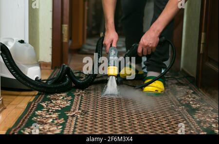 The process of cleaning carpets with a steam vacuum cleaner. An employee of a cleaning company cleans the carpet using steam. Stock Photo