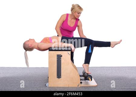 A 20-year-old female trainer practices Pilates on an elevator chair,  lifting her leg high above her head. A woman rests on her knee and hands  Stock Photo - Alamy