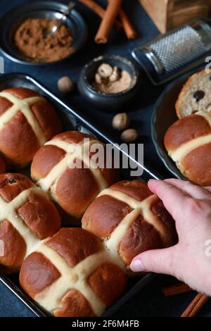 Freshly baked homemade Hot Cross Buns with spices on dark blue background with hand reaching in to take one Stock Photo