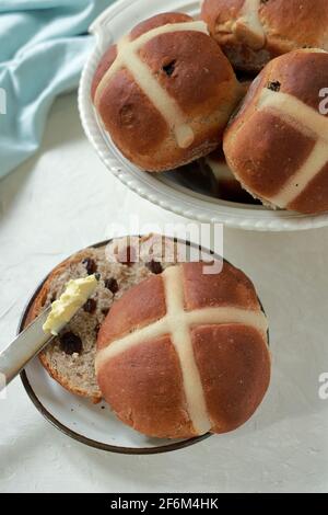 Freshly baked homemade Hot Cross Buns piled into a dish with one split open ready to be spread with butter Stock Photo