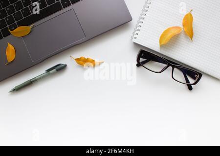 Autumn Flat lay, laptop keyboard, notebook, glasses, pen and yellow autumn leaves on white background.  Stock Photo