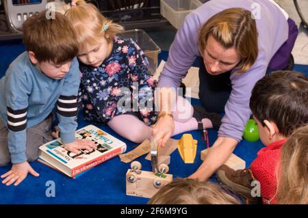 Kindergarten science class independent school female teacher demonstrating to small group how to hammer nails into vehicles they are constructing Stock Photo
