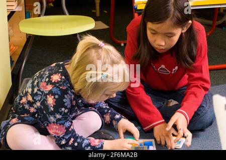 Independent elementary school Grade 4 and Kindergarten buddies two girls playing game, the older one assisting the younger one