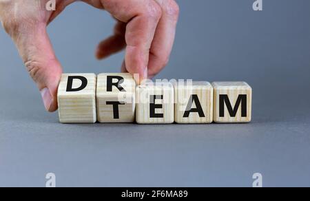 Dream team symbol. Businessman turns cubes and changes the word 'dream' to 'team'. Beautiful grey table, grey background. Business and dream team conc Stock Photo