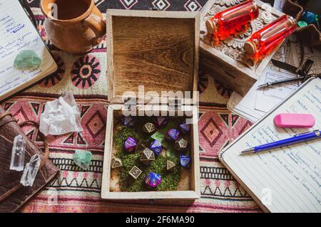 An image of an open wooden box with metallic and plastic purple role-playing dice surrounded by notebooks, crystals, and pen and paper on a textured pl Stock Photo
