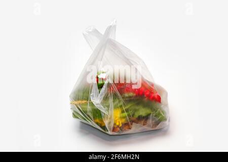 DEFOCUS. Plastic plant. Red and green plants flowers in a plastic bag on a white background. A dry blade of grass sticks out. Ecological problems. Out Stock Photo