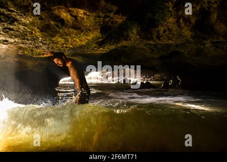 Attractive man with tattoos standing in spectacular Mermaid Caves with waves crashing on volcanic rocks, at Nanakuli Beach Park, Oahu, Hawaii, USA Stock Photo