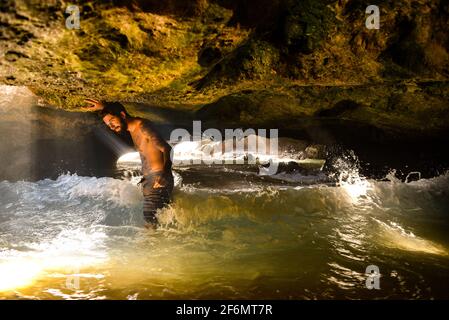 Attractive man with tattoos standing in spectacular Mermaid Caves with waves crashing on volcanic rocks, at Nanakuli Beach Park, Oahu, Hawaii, USA Stock Photo