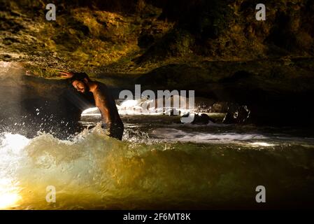 Attractive man with tattoos standing in spectacular Mermaid Caves with waves crashing on volcanic rocks, at Nanakuli Beach Park, Oahu, Hawaii, USA Stock Photo