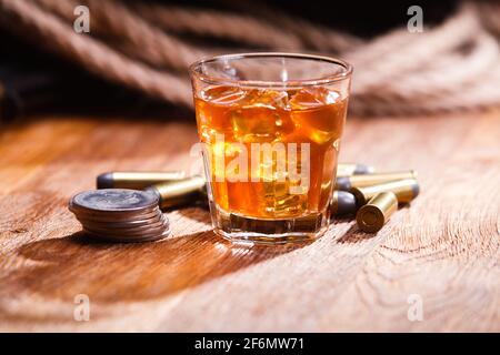 Glass of whisky and ice with ammunitions with old silver dollars coins on wooden bar table Stock Photo