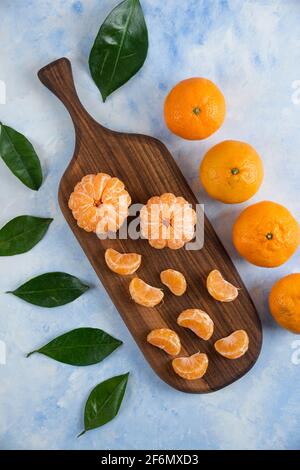 Peeled fresh mandarin slices on wooden board with whole mandarins Stock Photo