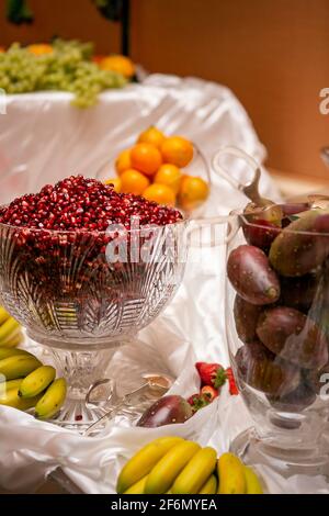 Table full of fruits in containers with pomegranate seeds, oranges, pricky pears, bananas, strawberries and grapes, catered for a wedding ceremony Stock Photo