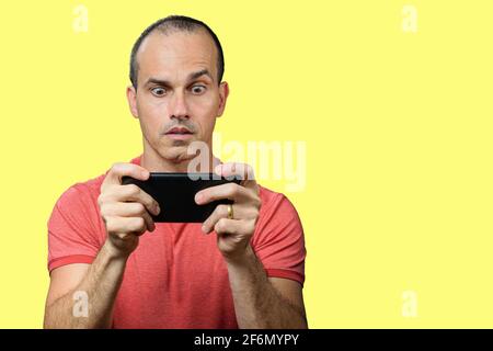 Mature man in casual clothing, wide-eyed and holding smartphone horizontally. Stock Photo