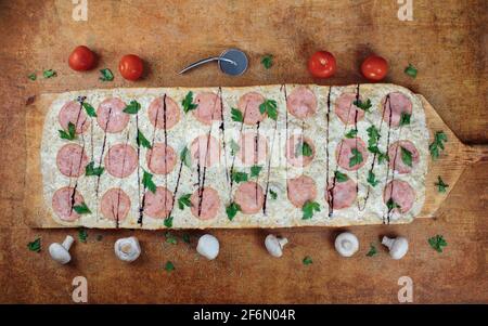 Long pizza with ham and herbs lies on a wooden table. Roman pizza on a wooden spatula. The pizza is one meter long. On a wooden pizza spatula. Stock Photo