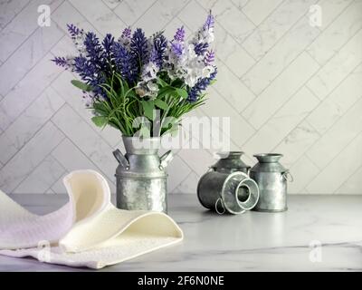 Rustic metal milk can filled with artificial purple lavender and lilacs for a simple spring country home decor with still life photography and a marbl Stock Photo