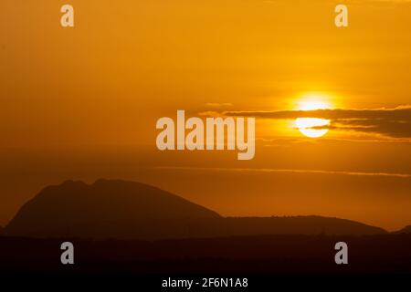 Silhouette of hills against beautiful golden hour sunset amidst a streak of clouds and beautiful orange sky Stock Photo