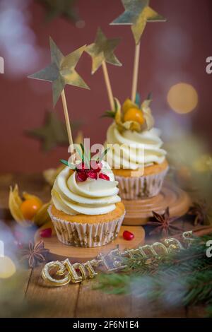 Christmas cupcakes with vanilla frosting, cranberries and rosemary on wooden background Stock Photo