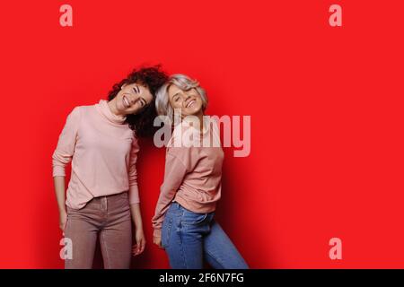 Lovely cheerful caucasian sisters with curly hair are smiling on a red studio wall with free space advertising something Stock Photo