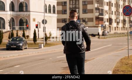 Back of a man with a black backpack. A man rides an electric scooter Stock Photo