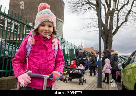 Five year old girl outside school at home time, on a scooter Stock Photo