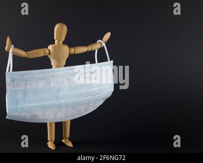 Disposable face mask for health care and for helping slow the spread of the coronavirus. Wooden figure of man holds surgical mask by the ear loops Stock Photo