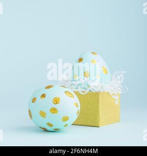Elegant easter eggs with gold dots and golden gift box on blue background, square. Stock Photo