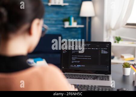 Young developer programming software typing html code deloping application for mobile use. Student working at infographics javascript using laptop computer while sitting at desk in living room Stock Photo