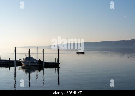 A view of a calm blue lake with moored ship and a small motorboat cruising through the water Stock Photo