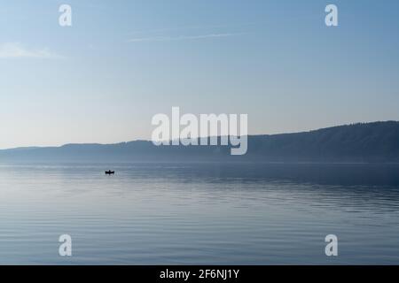 A view of a calm blue lake with a small motorboat cruising through the water Stock Photo