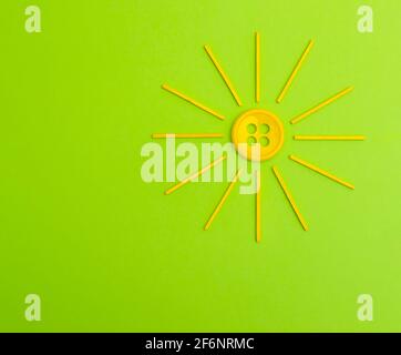 Stylized Yellow sun made from button and wood sticks on a green background. Creative spring flat lay. Stock Photo