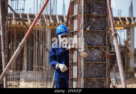 Aktau, Kazakhstan - May 19, 2012 Construction of modern asphaltic bitumen plant. Worker in white balaclava mask, and blue helmet assembling forms for