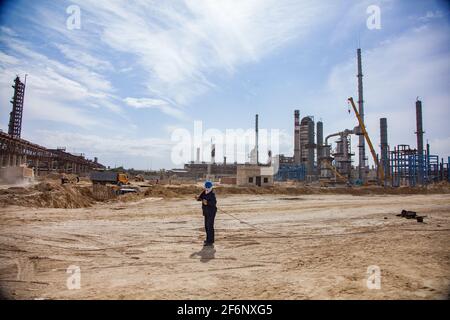 Aktau, Kazakhstan - May 19, 2012 Construction of modern asphaltic bitumen plant. Worker in balaclava mask with steel rope on sand. Refinery plant on b