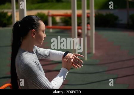 Young athletic woman checking her fitness tracker, pulse and heart rate, lost calories during outdoor workout Stock Photo