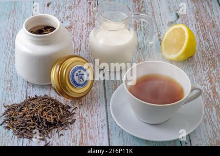 Tea leaves ready for infusion, white cup with tea infusion, lemon cut in half, jug with milk and white bottle containing tea inside. The lid that rest Stock Photo