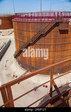 Rusted oil storage tanks on blue sky background. View from tank's roof. Asphaltic bitumen plant. Stock Photo