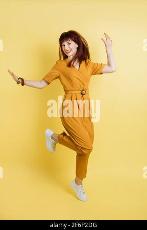 People, emotions, fun and joy. Full length portrait of crazy excited joyful pretty young lady in yellow overalls and sneakers, having fun and jumping on isolated yellow background. Stock Photo