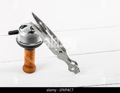 Brown ceramic hookah bowl with metal lid and tongs on a white wooden background. Stock Photo