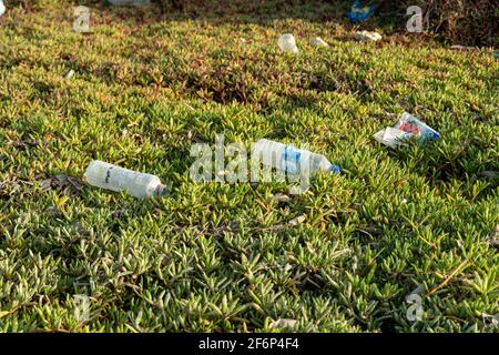 Plastic garbage pollution side view on grass near waters showing discarded trash and bottles for environmental concepts. Stock Photo