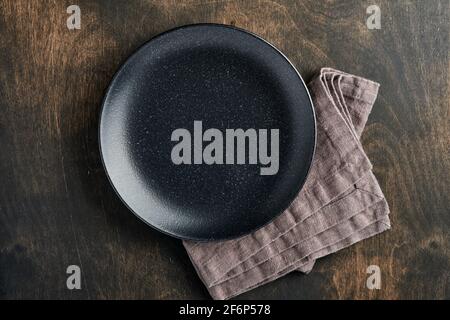 Empty black plate, cutlery and napkin on old wooden table top view. Table setting. Stock Photo