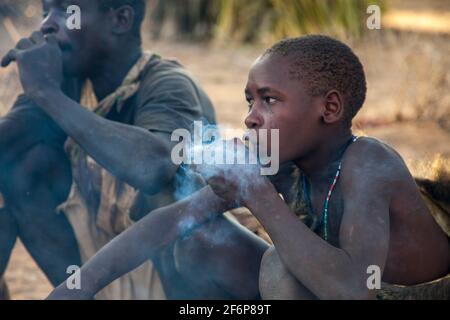 (10/15/2014) The Hadza are used to socialize around the fire by smoking a pipe or playing tribal instrumentsThe Hadza are a Tanzanian ethnic group living around Lake Eyasi.  The population reaches almost a thousand people; 300-400 live as hunter-gatherers.  The Hadza have no close correlation with any other population. They were considered an East African branch of the Khoisan people, mainly due to the fact that their language has the typical pops of the Khoisan languages, but recent genetic research studies suggest a proximity to the Pygmies. Their language appears to be isolated, unrelated t Stock Photo