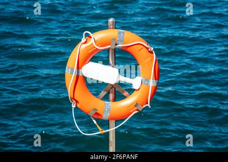 SOS nautical emergency concept. Lifebuoy, orange lifebelt put on silver vertical iron ready for using. Close up circle lifesaver buoy at Marina Flisvo Stock Photo