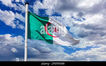 Algeria flag, Algerian national symbol on a flagpole waving against blue cloudy sky Stock Photo