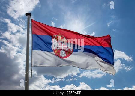 Serbia flag, Republic of Serbia national symbol on a flagpole waving against blue cloudy sky Stock Photo