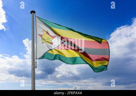 Zimbabwe flag, Republic of Zimbabwe national symbol on a flagpole waving against blue cloudy sky Stock Photo