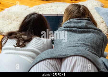 two young women lying on the floor and staring at a laptop screen, rear view Stock Photo